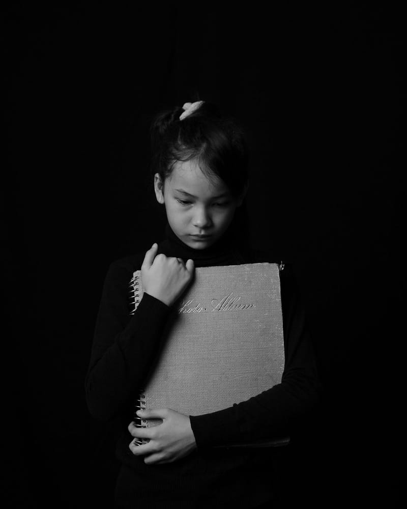 A young girl in black and white, looking down and hugging a photo album to her chest